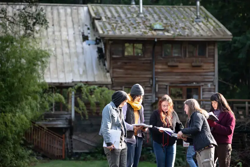 a group of students outside the farmhouse looking at their notes with a professor