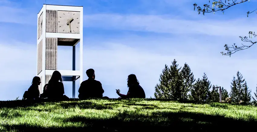 siloueted students sitting on the grass with the clocktower in the background