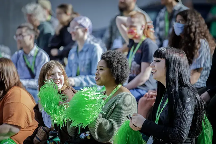 Group shot of students celebrating at an orientation event and cheering with green pom-poms