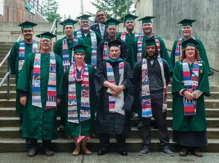 A group of graduating veterans posed wearing green caps and gowns with colorful handmade stoles