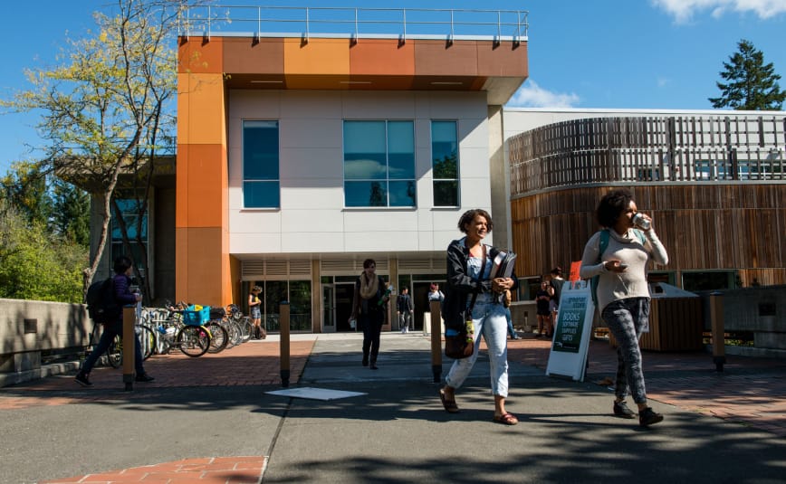 Two female students walk out of a building with an orange roof, away from the camera.