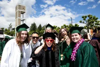 Graduates smiling at the camera, wearing graduation regalia in white, black and green