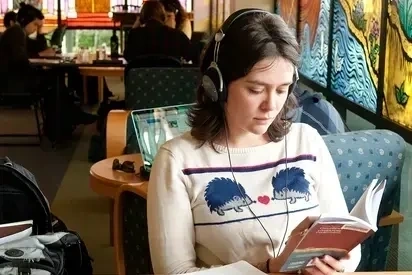 A student reads in the library while other students study in the background