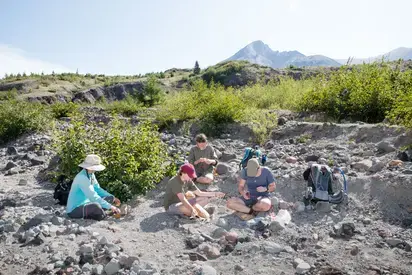 a group of students sitting outside in the dirt doing stream research