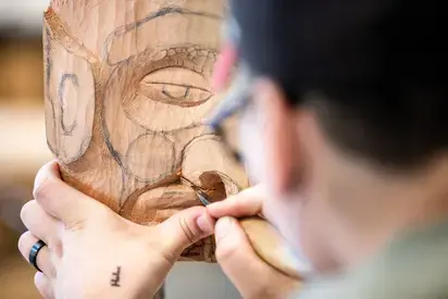 the back of a students head, looking over their shoulder at a wood carving they are working on