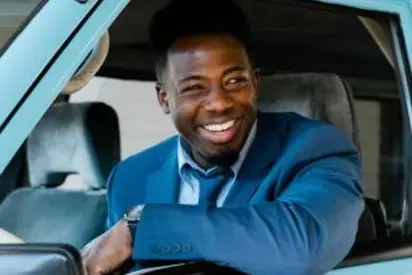 smiling man in blue blazer and tie driving a light blue van