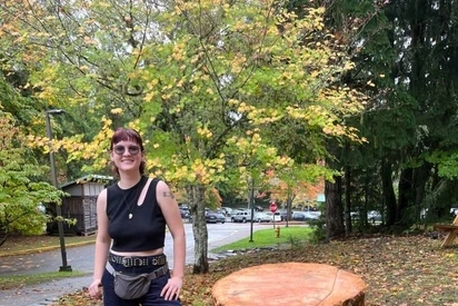 Aubrey Evelo standing behind large tree stumps for a honeybee hive project