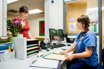A nurse and hospital adminstrator speak with each other at the check in desk of a medical office