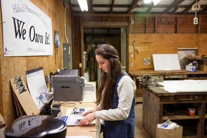 A person organizes papers in a nonprofit organziation office, with a large sign above their head that reads We Own It
