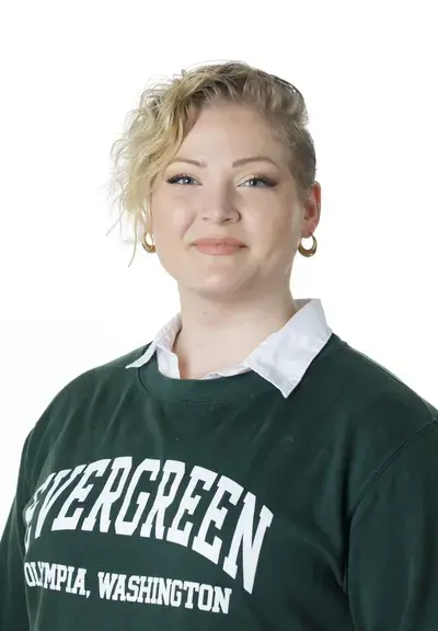 a photo of a white woman with short wavy blond hair wearing an evergreen crewneck sweater smiling at the camera