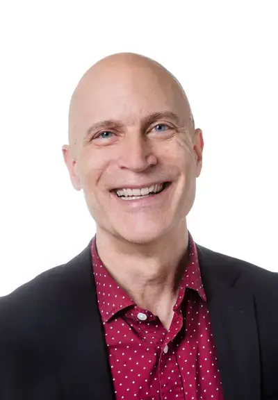 a white man smiling at the camera and wearing a red polka dot button down and a black blazer