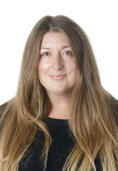 a woman with long brown hair looking at the camera, they are wearing a black shirt