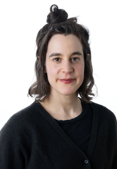 Headshot of person with sholder length dark hair wearing a black shirt against a white background