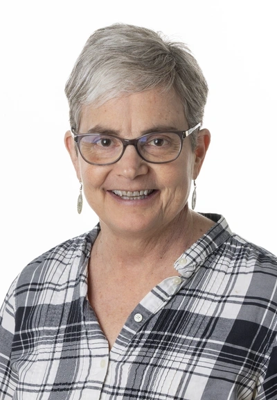 headshot of person with short grey hair, glasses and a black and grey plaid button down shirt.