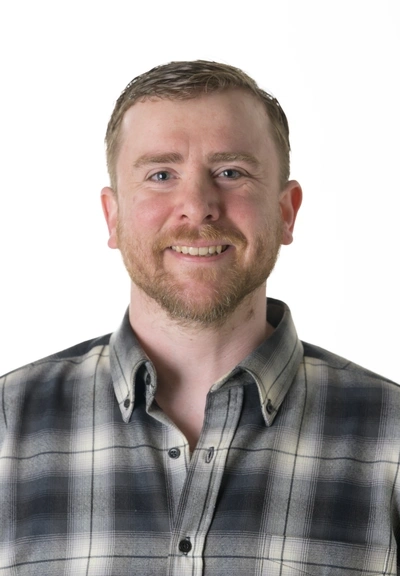 head shot of a person with short hair and a very short beard wearing a grey plaid shirt