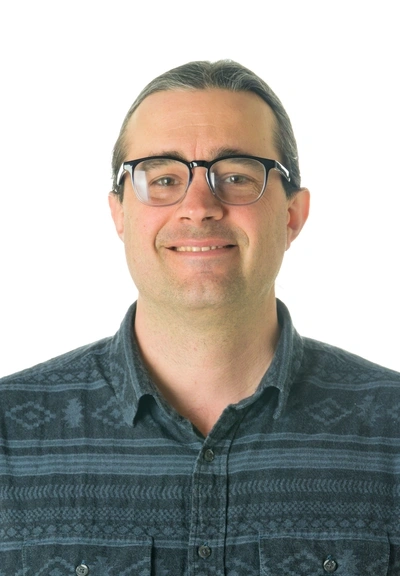 Headshot of person with short dark hair and glasses wearing a blue stripped and patterend button down shirt