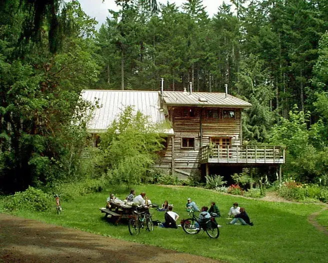 an old film photo of the farm house from the archives. a group of students are sitting in the grass in front of the farm house