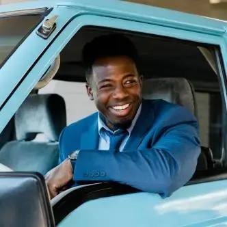 smiling man in blue blazer and tie driving a light blue van
