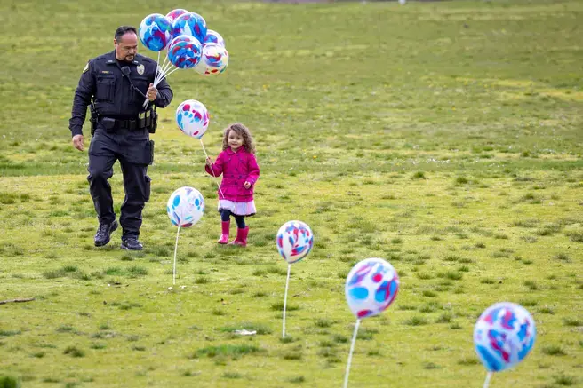 A police officer gathers balloons with a young child on a grassy field