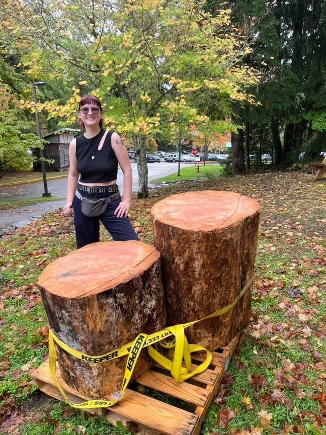 Aubrey Evelo standing behind large tree stumps for a honeybee hive project