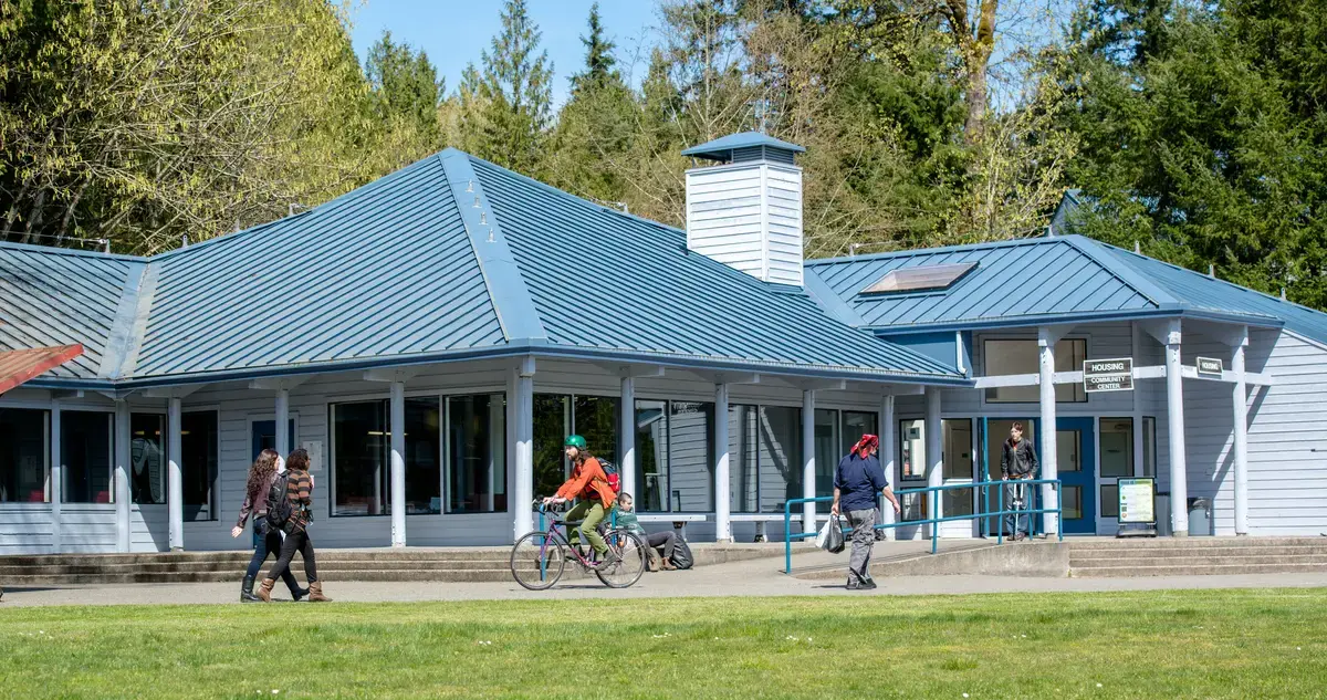 students ride bikes in front of the housing community center on a spring day