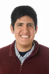 a man with light brown skin and short black hair smiling at the camera, he is wearing a maroon quarter-zip sweater