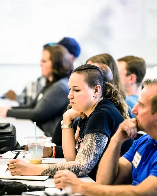 Group of students in a row down a table listen to a lecture