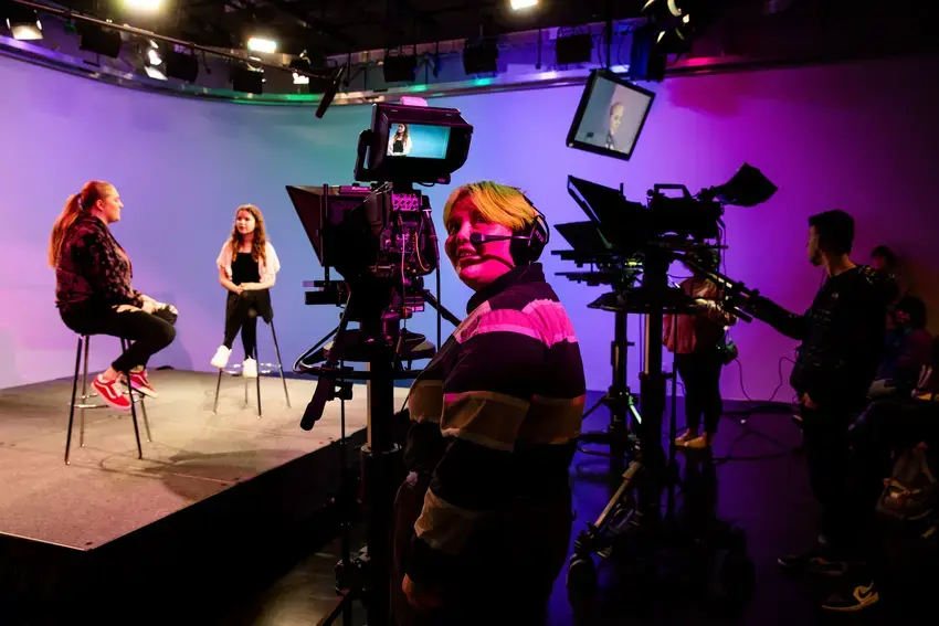 a student behind the camera in CCAM, looking back and smiling with purple and pink lights over them