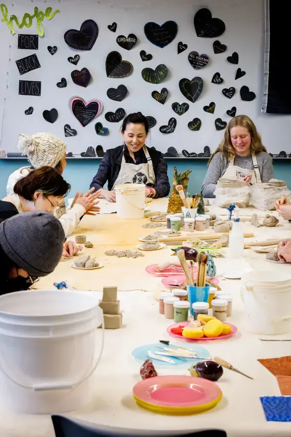 A group of people around a table filled with craft supplies and a wall full of paper hearts on the wall behind them