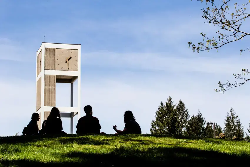 Group of siloueted student sit on the round with the clocktower in the background