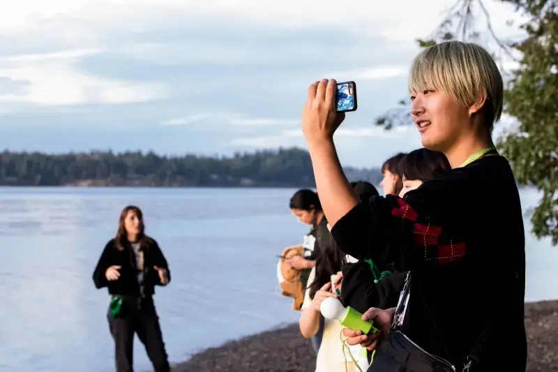 A student takes a photo with their phone at the Evergreen beach