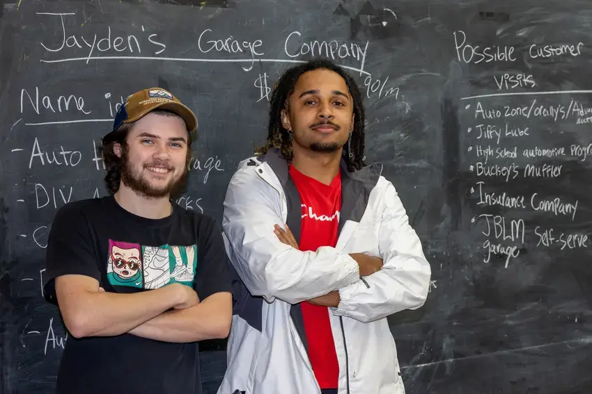 two students standing next to each other with their arms crossed in front of a chalkboard
