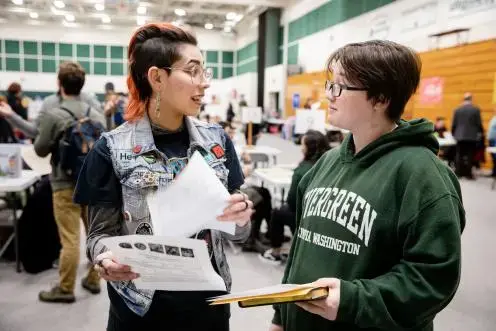 Students conversing while holding papers in an event space