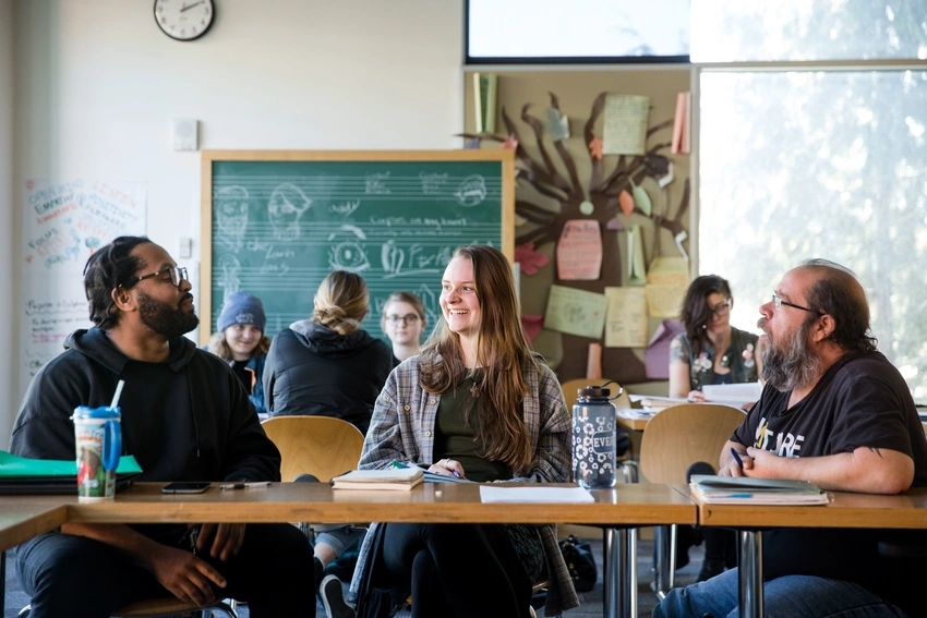 three students sitting in a classroom talking together