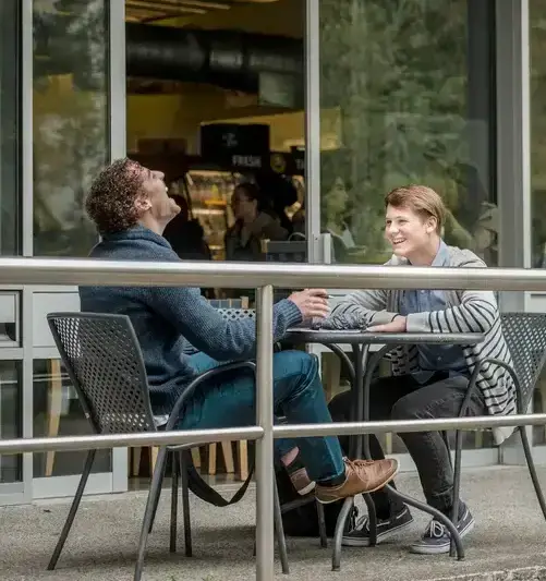 Two students talking and laughing sit at a table in front of einstiens bagels 