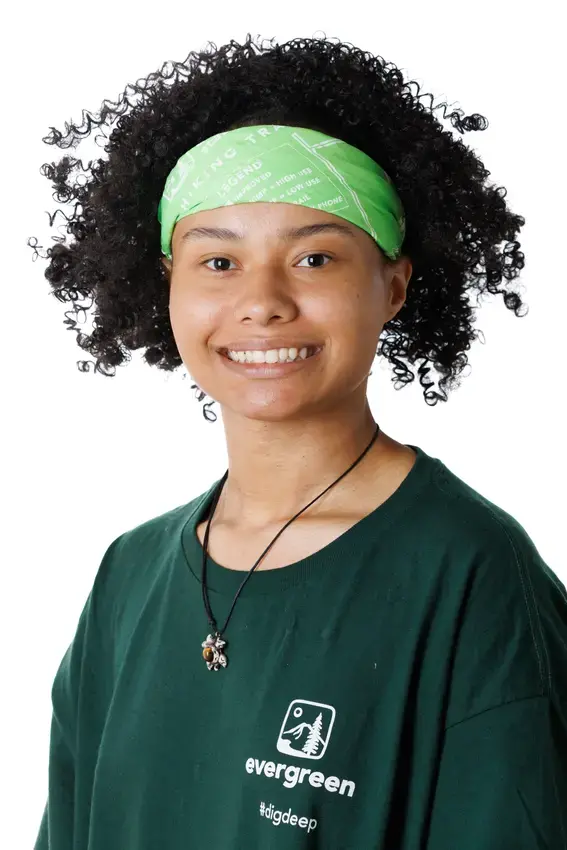 A person with long very curly hair and a green headband looks directly at the camera