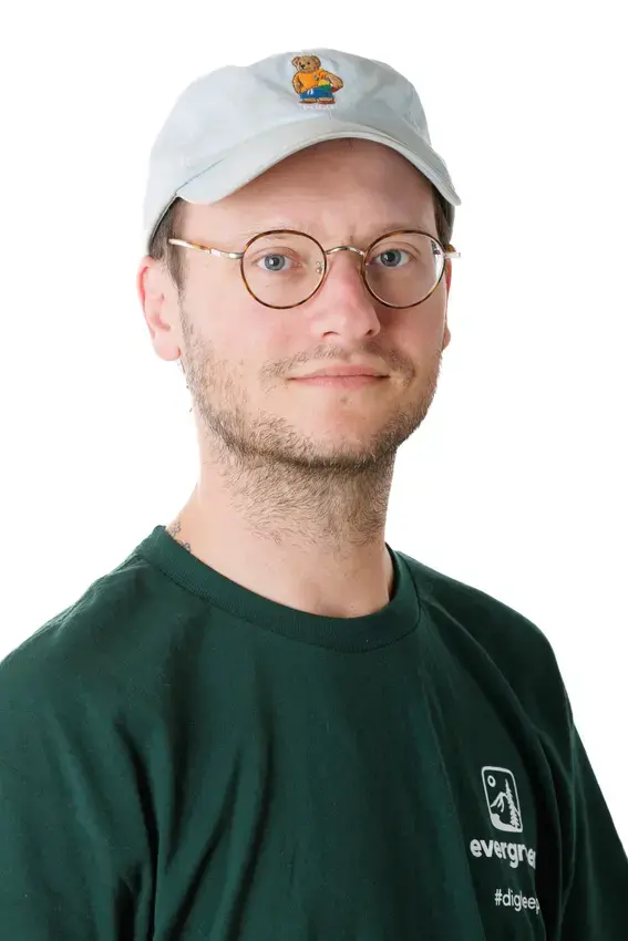 A person with glasses and a white ball cap with a teddy bear on it looks directly into the camera