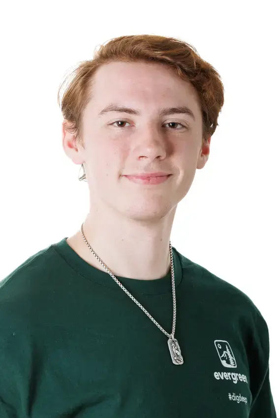 A person with red hair wearing a long necklace looks directly into the camera