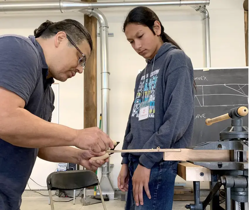 Wood carver demonstrating a technique to younger person