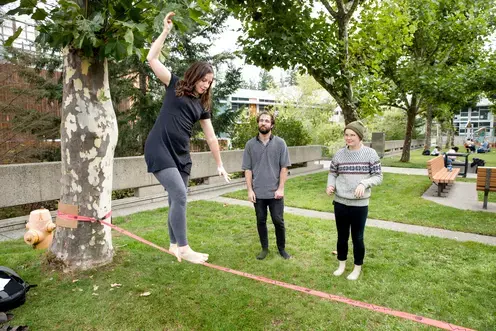 Two students watch another student practicing slackline