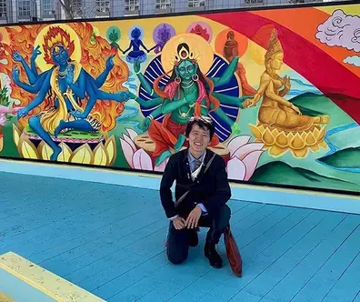 Dr. Tenzin by a Tibetan Buddhist mural