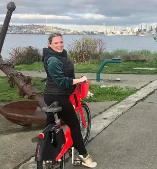 Christine Carlson standing over a bike at a waterfront park in Seattle overlooking the skyline.