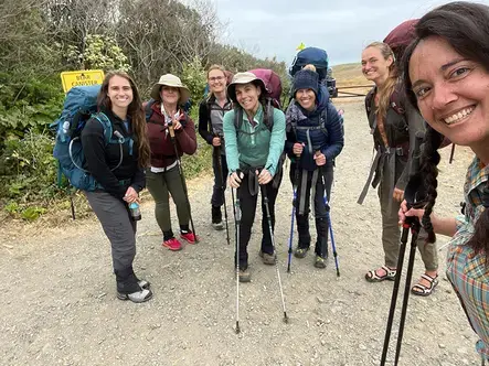 Natalie Pyrooz and Sierra Wagner pose for a photo with fellow woman hikers, carrying large travel packs and hiking poles, during one of their retreats. 