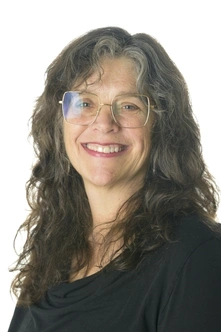 Person with long grey hair wearing large glasses and a dark top